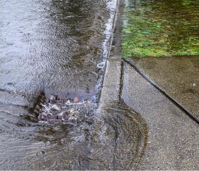heavy rain and flood waters flowing down a curb drain